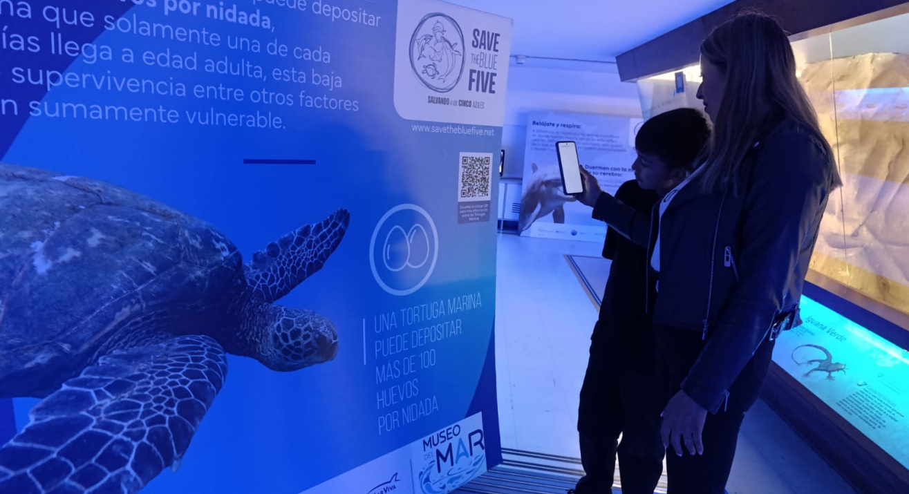 Una mujer y un niño leyendo un código QR en instalación de Save the Blue Five en el en el Museo del mar